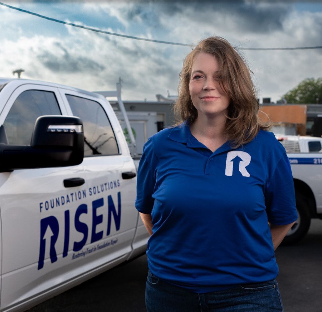 A woman in a blue shirt is standing in front of a white truck that says risen