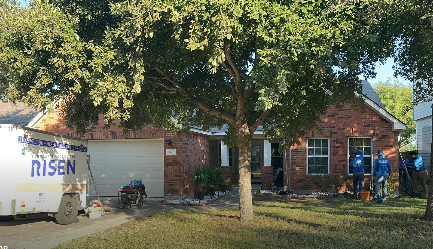 A white truck with the word risen on it is parked in front of a brick house.