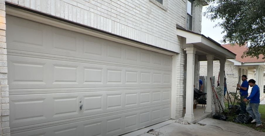 A group of men are standing in front of a white garage door.