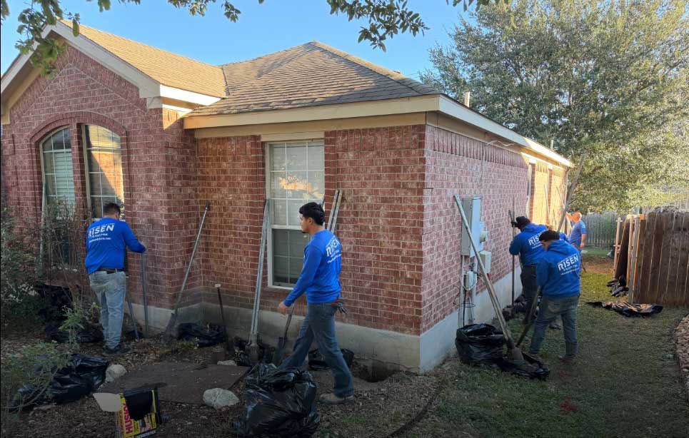 Construction workers in blue shirts are landscaping around a brick house.