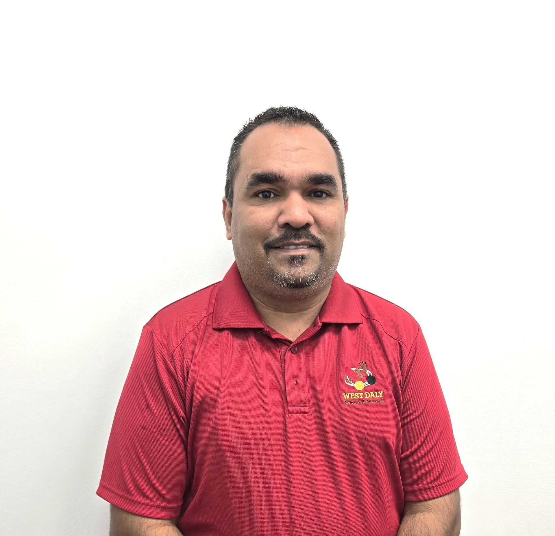 Man in blue shirt with a company logo, looking forward, against a white background.