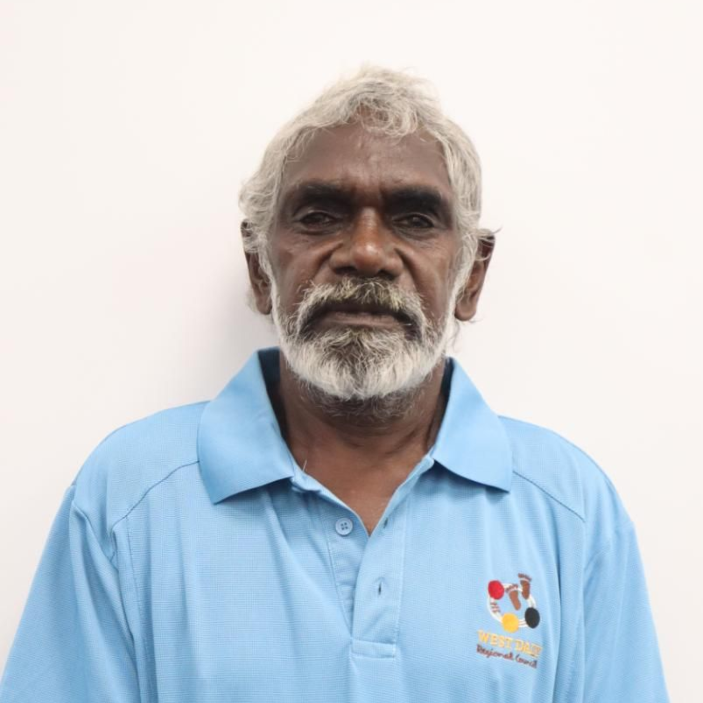Man with gray hair and beard wearing a blue shirt, facing forward.