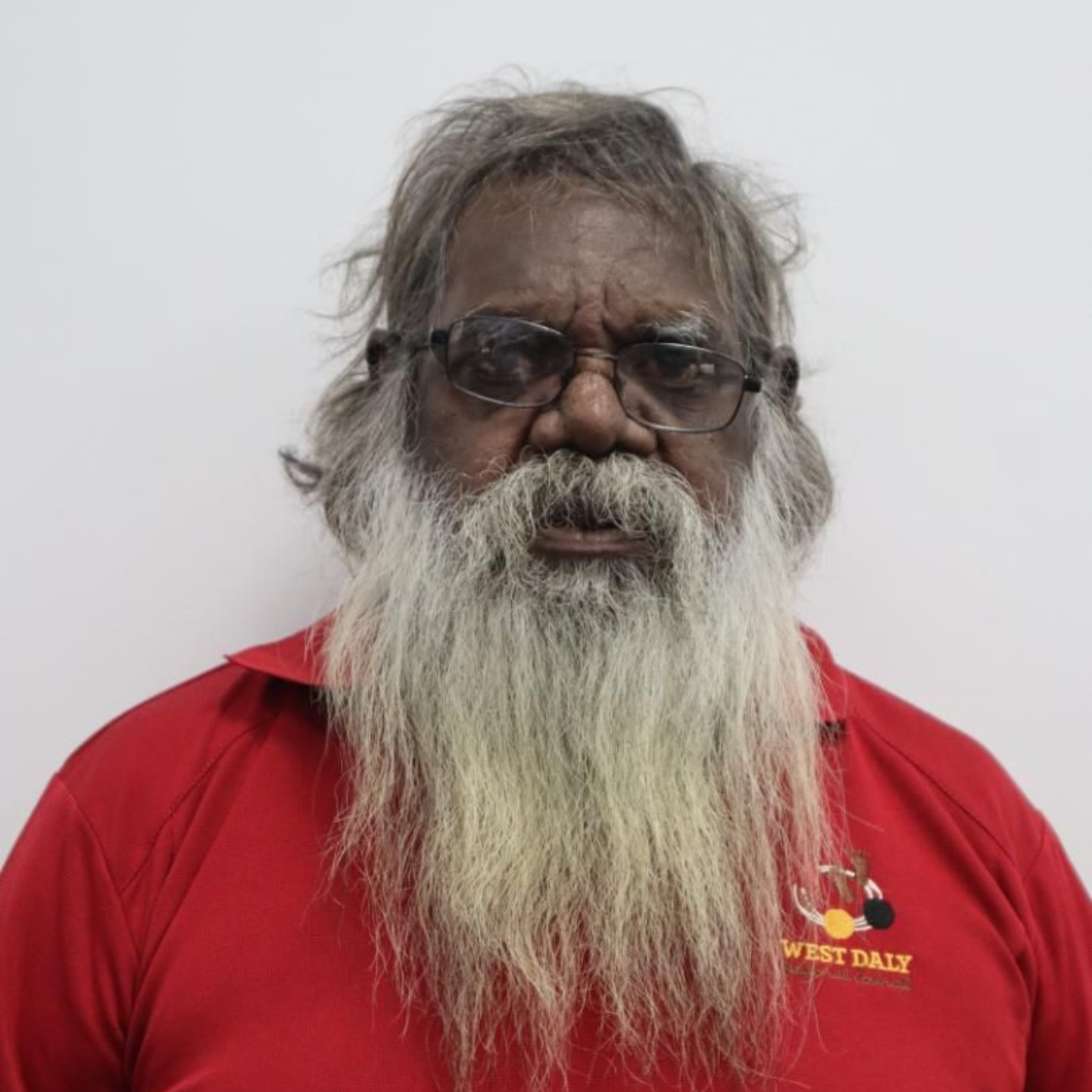 Man with long white beard and glasses wearing a red shirt, looking at the camera.