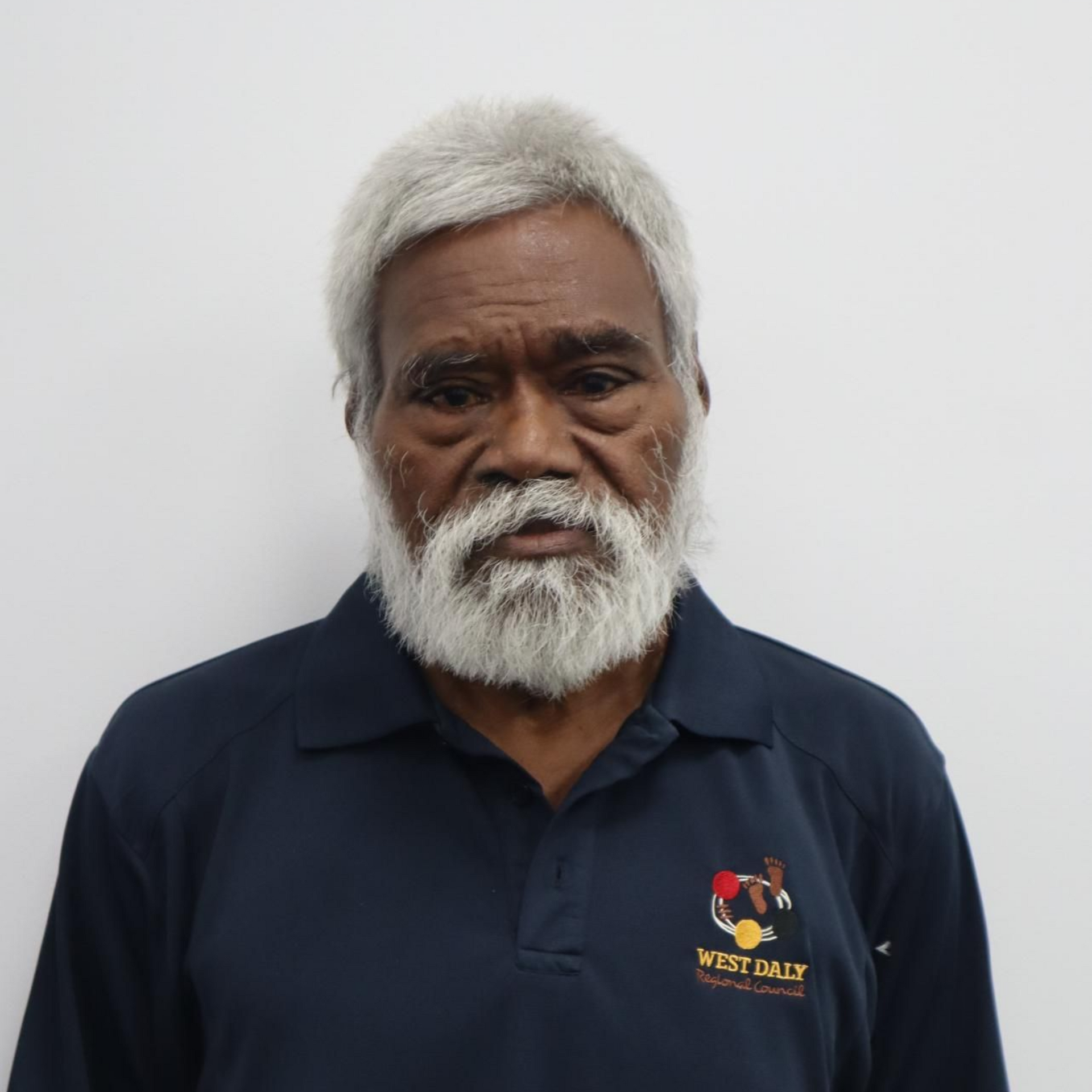 Man with gray hair and beard, wearing a navy polo shirt with 