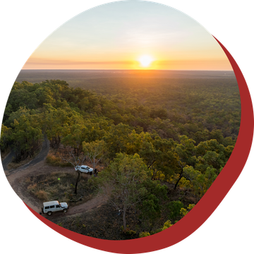 Sunset over lush green forest with two off-road vehicles on a dirt road.