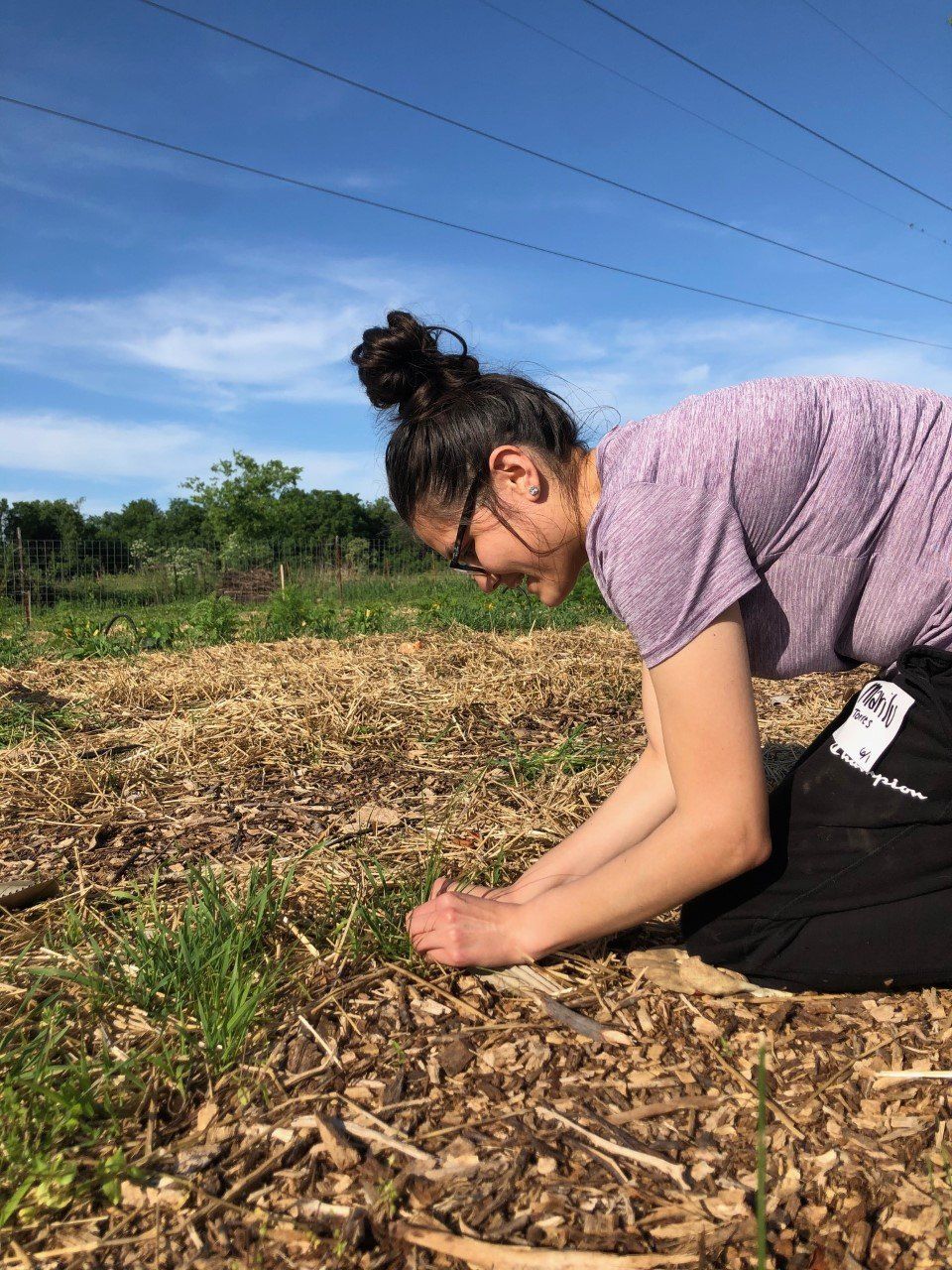 A woman is kneeling down in a field looking at a plant.