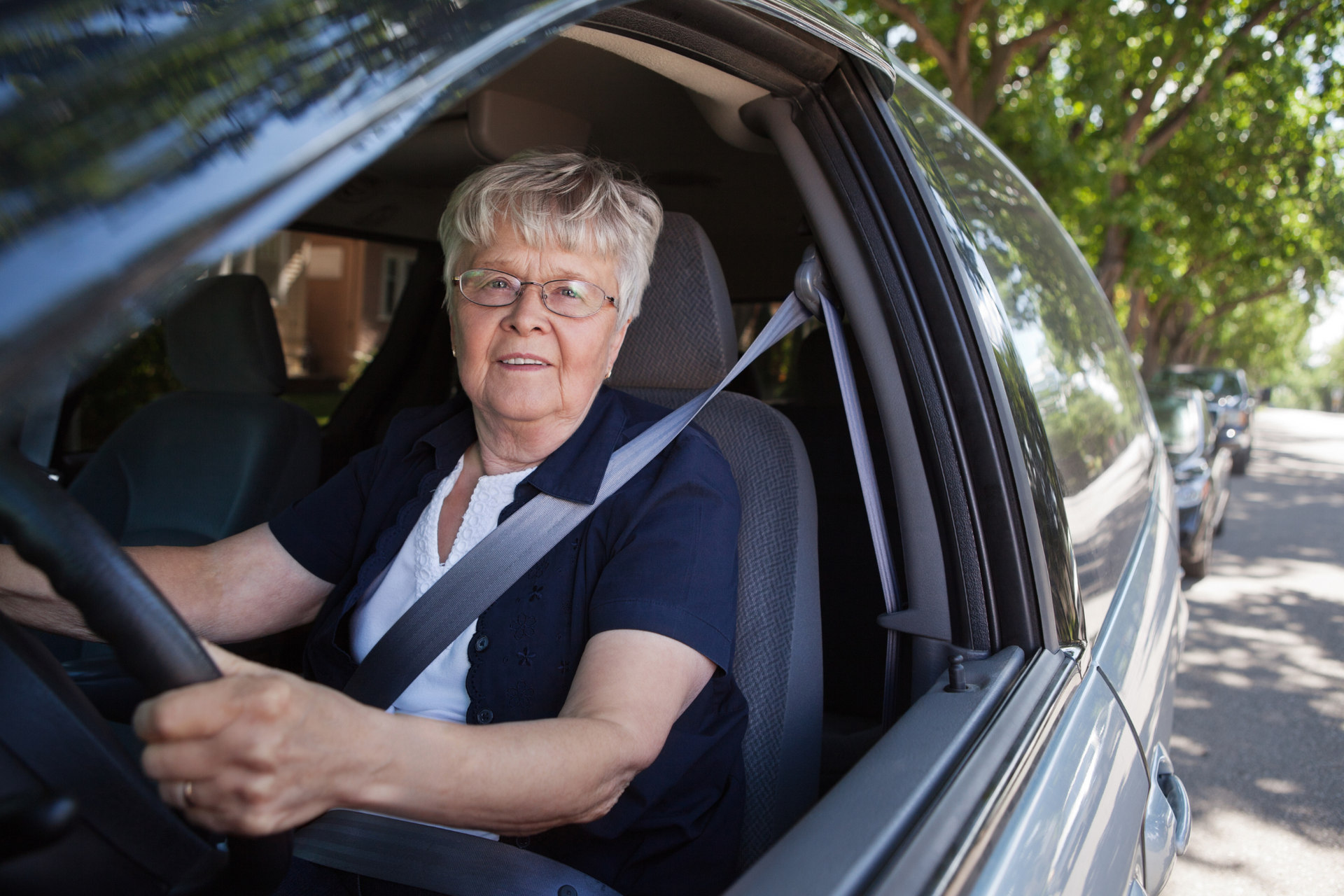 An elderly woman is sitting in the driver 's seat of a car.