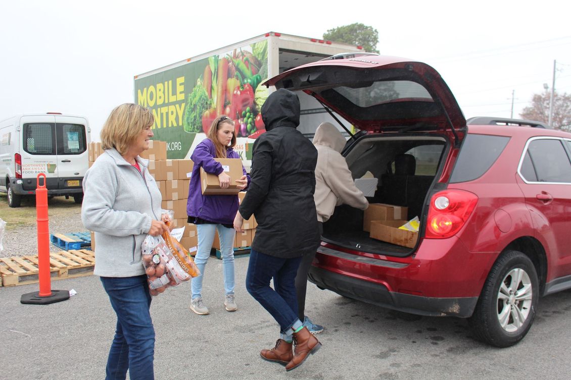 A group of people are loading boxes into the back of a red car.