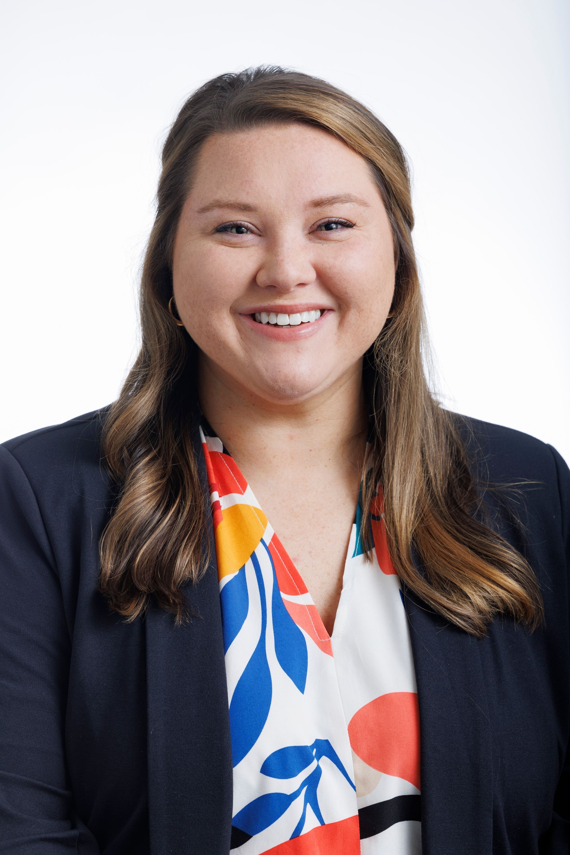 A woman in a colorful shirt and jacket is smiling for the camera.