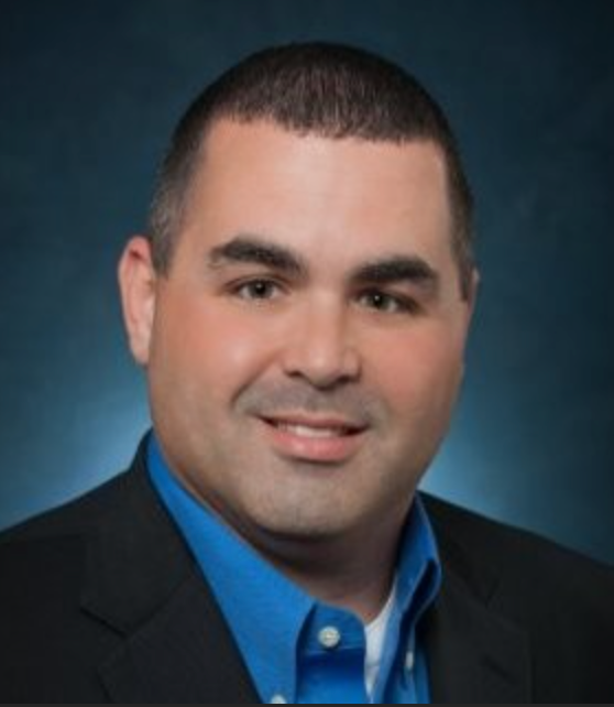 A man in a suit and white shirt is smiling for the camera.