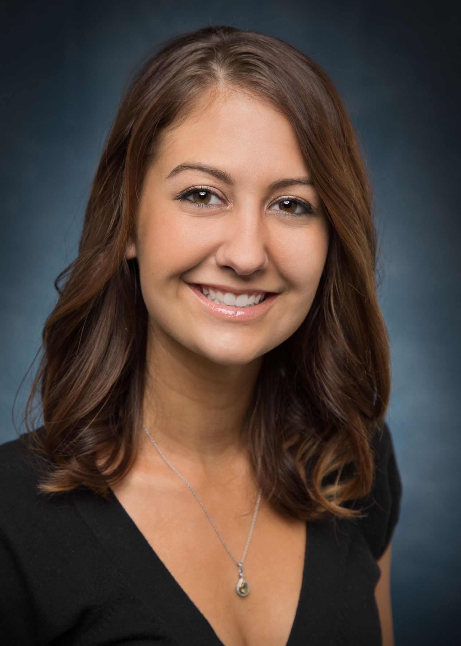 A woman wearing a black shirt and a necklace is smiling for the camera.