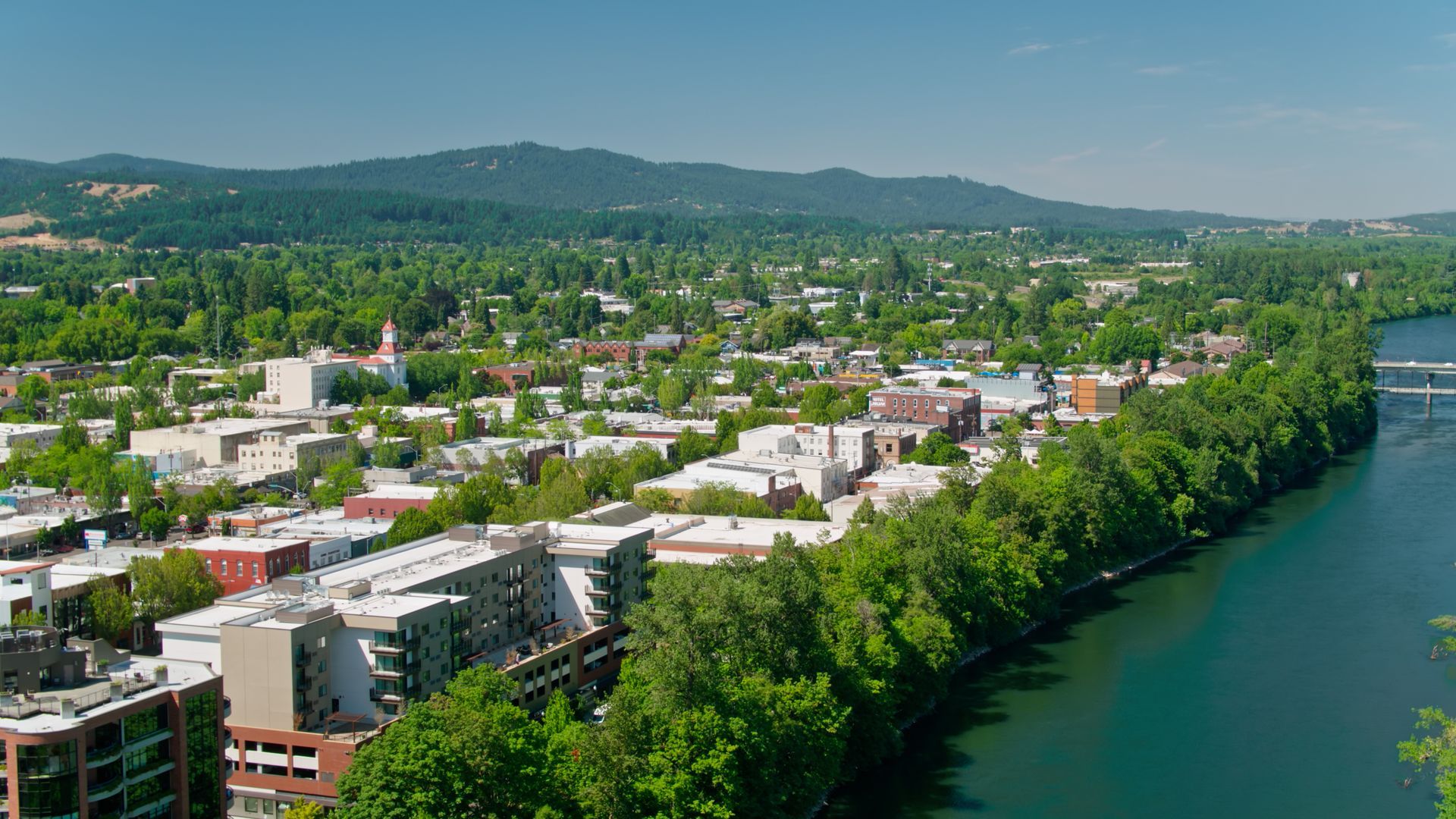 Townscape with buildings, trees, river, and hills under a bright blue sky Townscape with buildings, trees, river, and hills under a bright blue sky