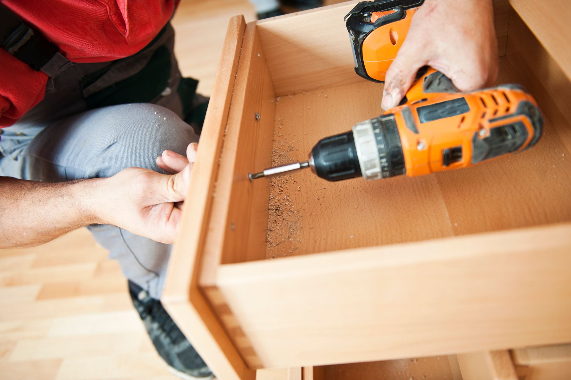 Person using an orange power drill to assemble a wooden drawer