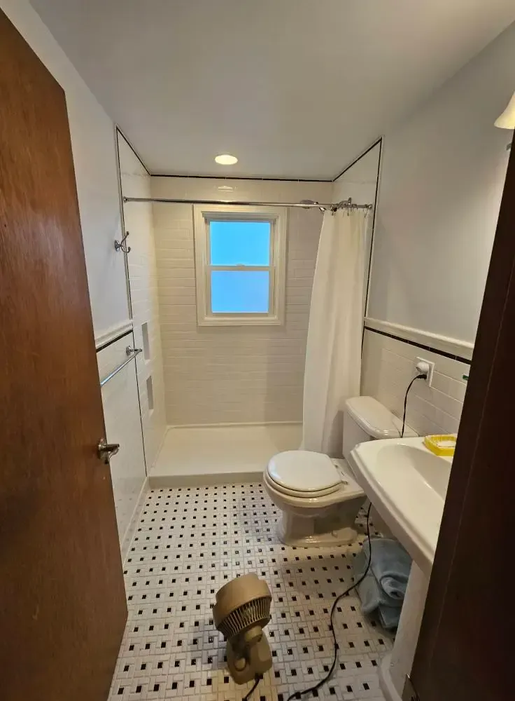 Bathroom with white and black tile, white shower and toilet, and wood door.