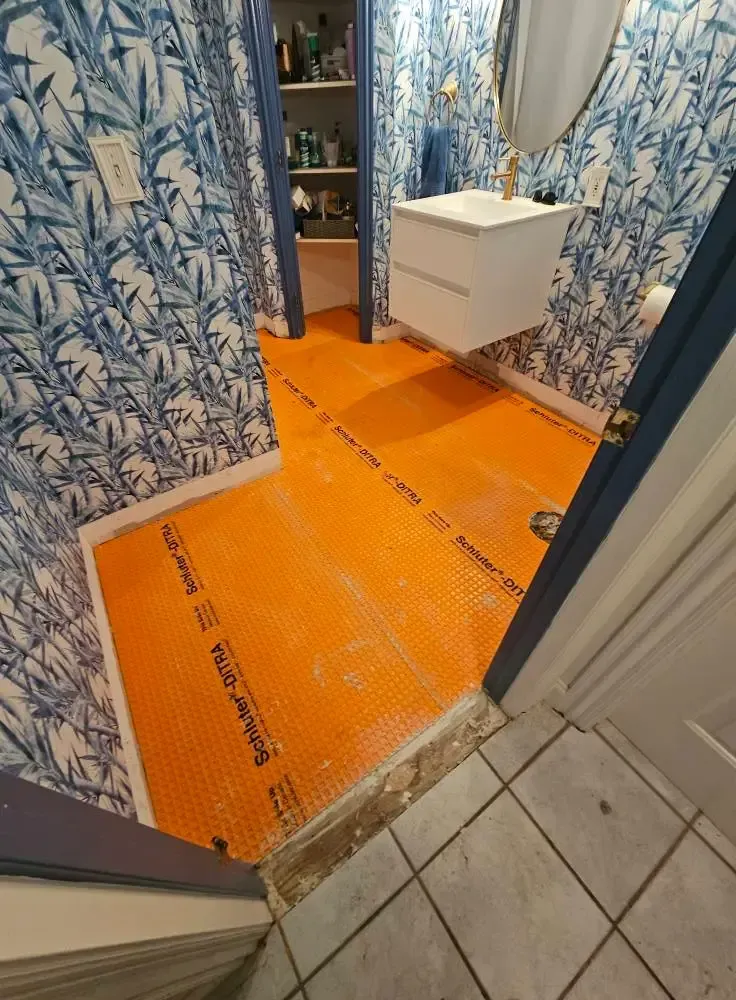 Bathroom renovation in progress; orange waterproofing membrane on floor; blue floral wallpaper; white floating vanity.