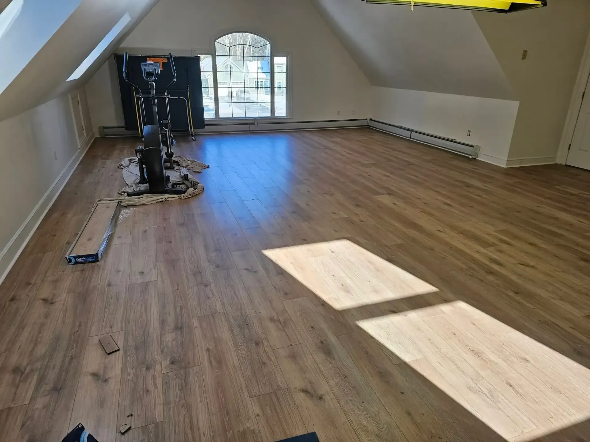 Attic room with new wood flooring; sunlight streams through arched window, illuminating the floor.
