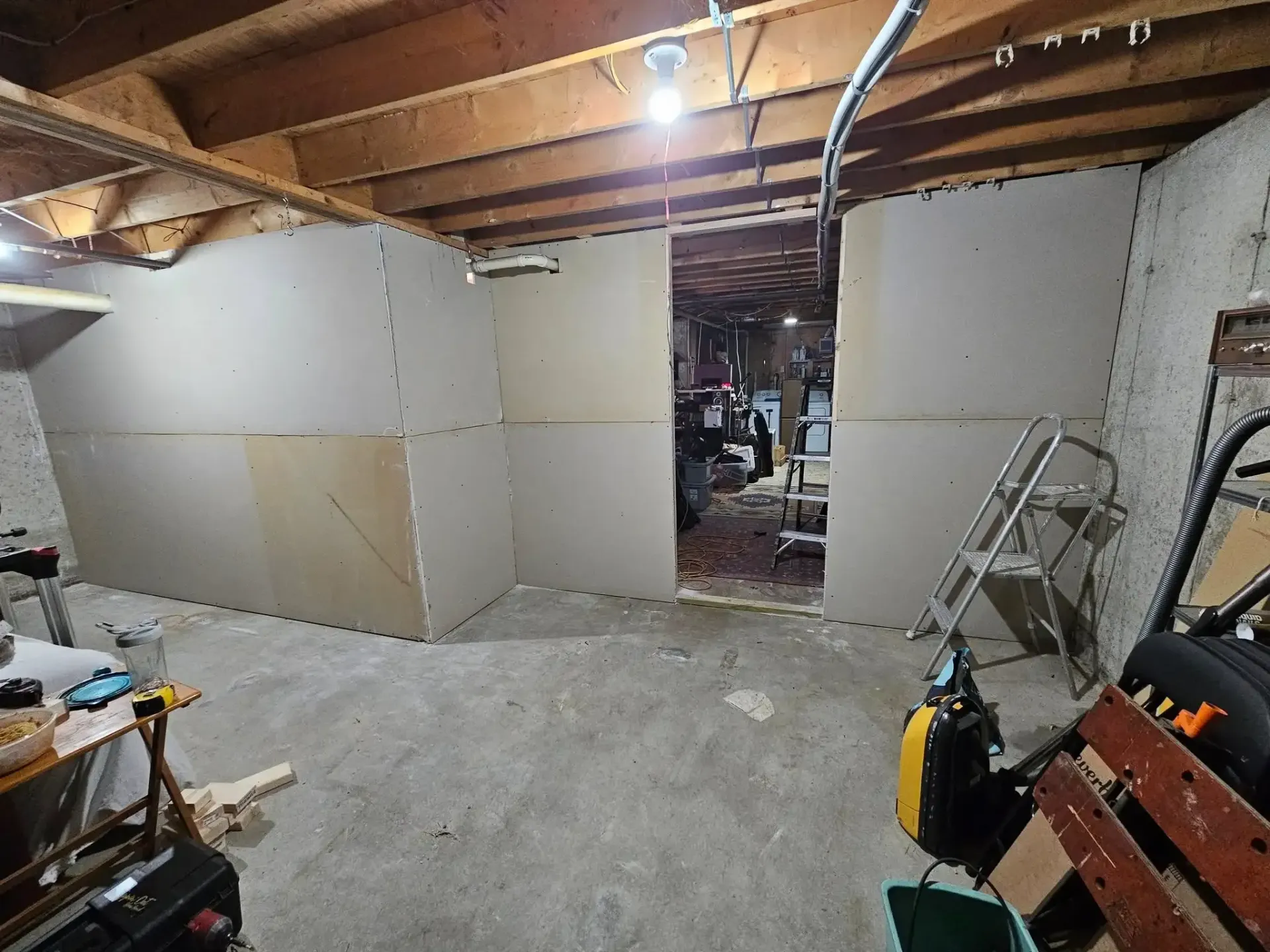 Basement with unfinished walls and an open doorway. Construction materials and tools are present.