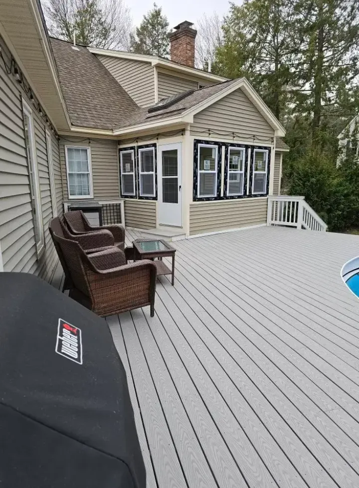A house with a gray deck, outdoor seating, and grill. The house has a porch with black framed windows.