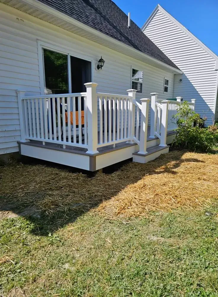 White deck with railing attached to a white house with a sliding glass door; dry grass in front.