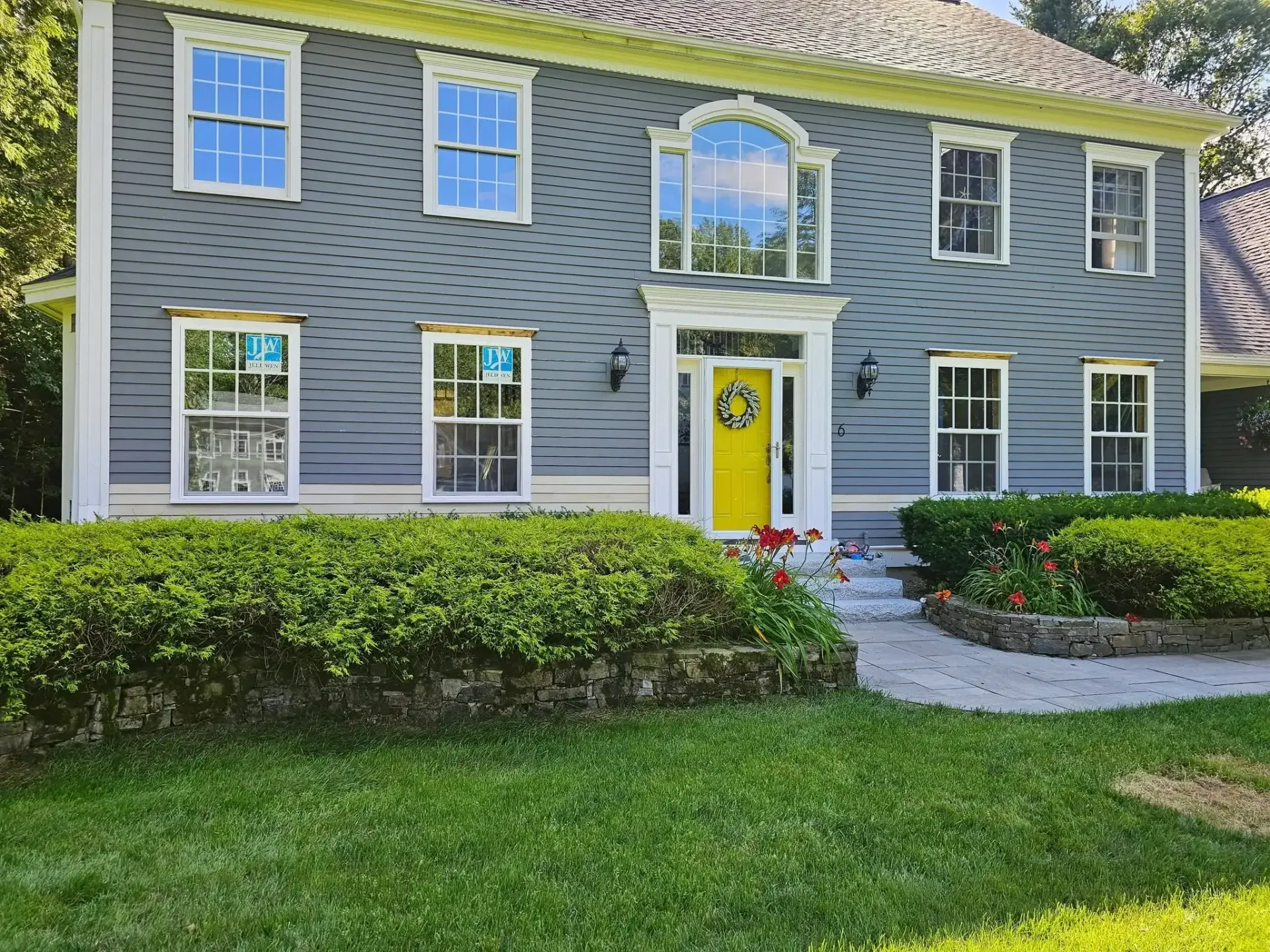Two-story blue house with white trim, yellow door, and manicured landscaping.