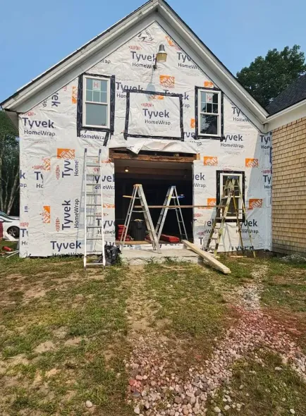 Building exterior under construction; Tyvek wrap, windows, ladder, open garage door.