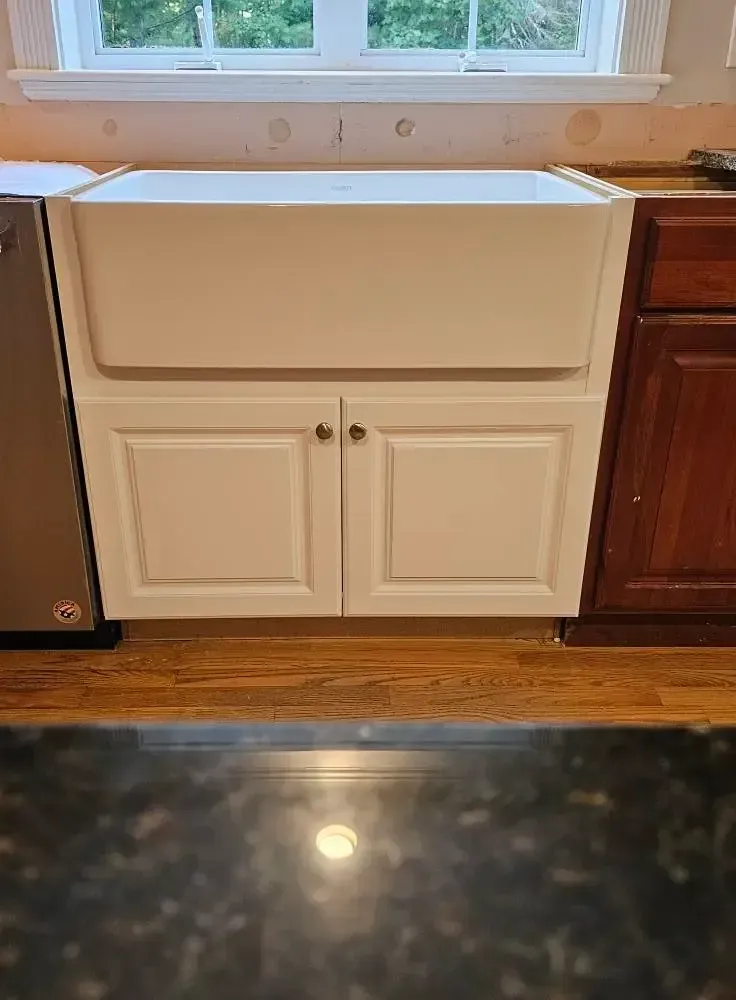 White farmhouse sink with cabinet below, set in a kitchen.