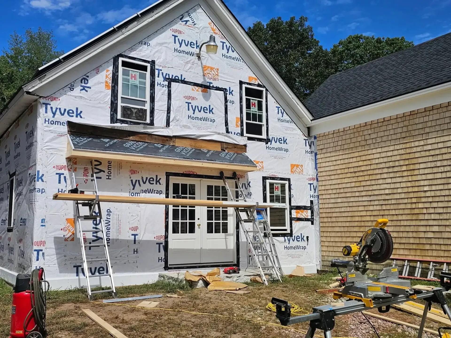 Building exterior under construction; covered in Tyvek, windows installed, scaffolding and tools visible.