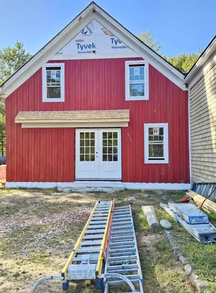 Red barn under construction with white windows and doors.