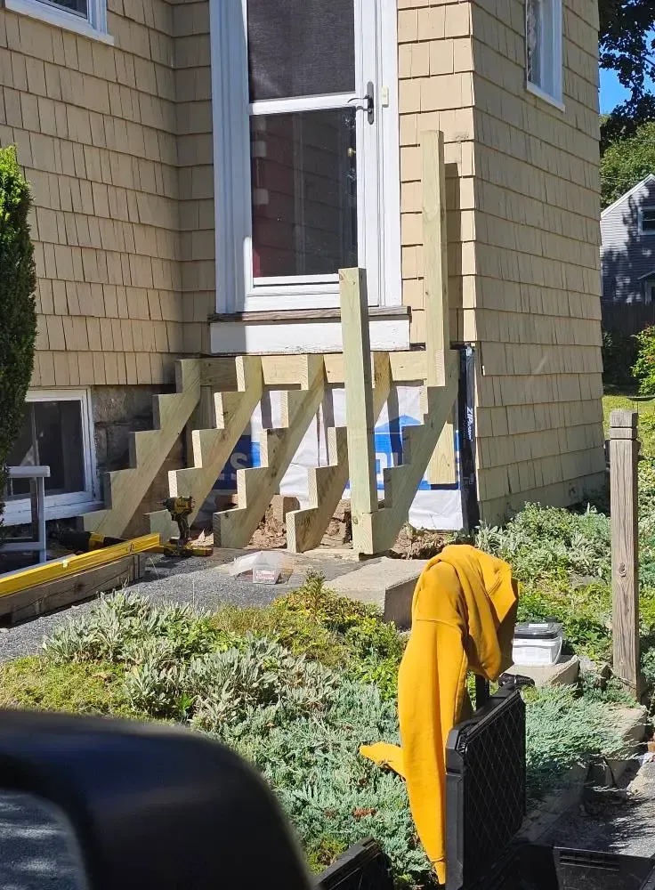 Wooden steps leading up to a house entrance; steps under construction; yellow jacket draped over a black fence.