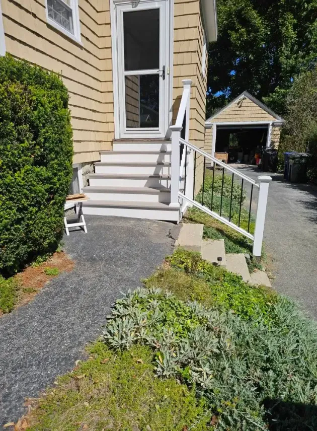 Exterior view of a house with steps leading to a front door and a driveway, with a garage in the background.