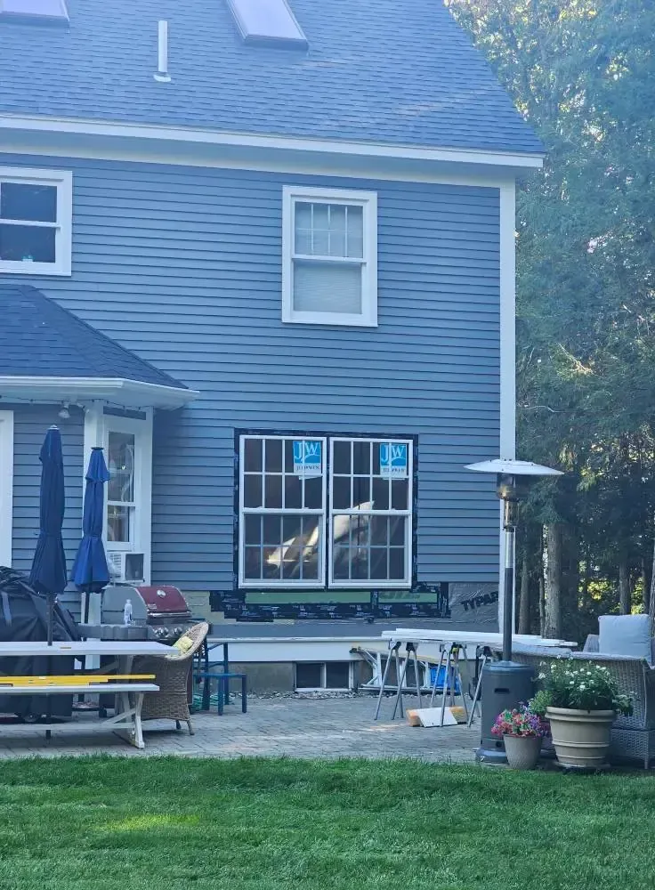 Back exterior of blue-sided house with new windows under construction. Patio furniture and a heater are in the yard.
