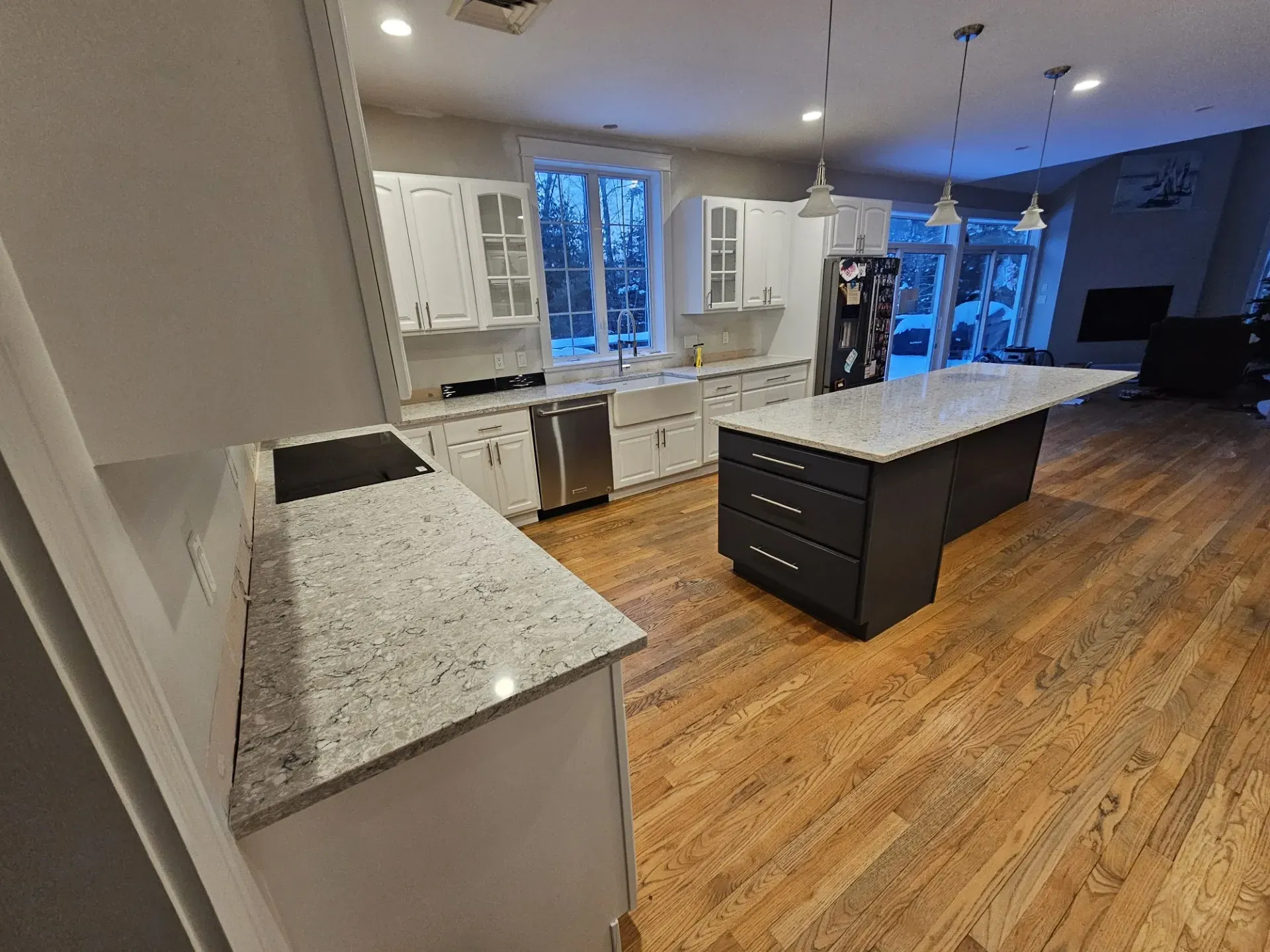 A modern kitchen featuring white cabinets, granite countertops, a dark island, and hardwood floors.