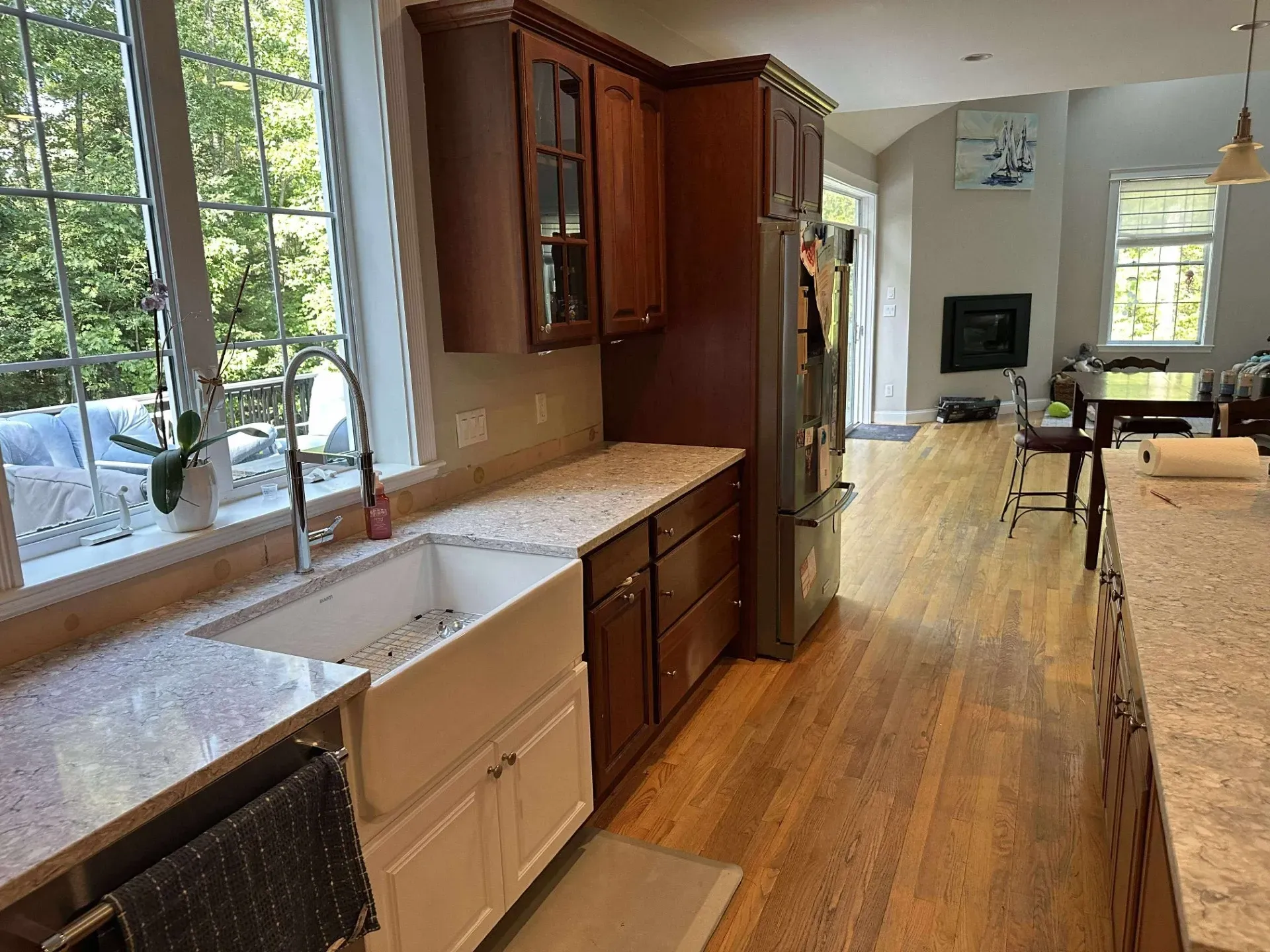 A kitchen with white farmhouse sink, granite countertops, cherry cabinets, and hardwood floors in an open-plan home.
