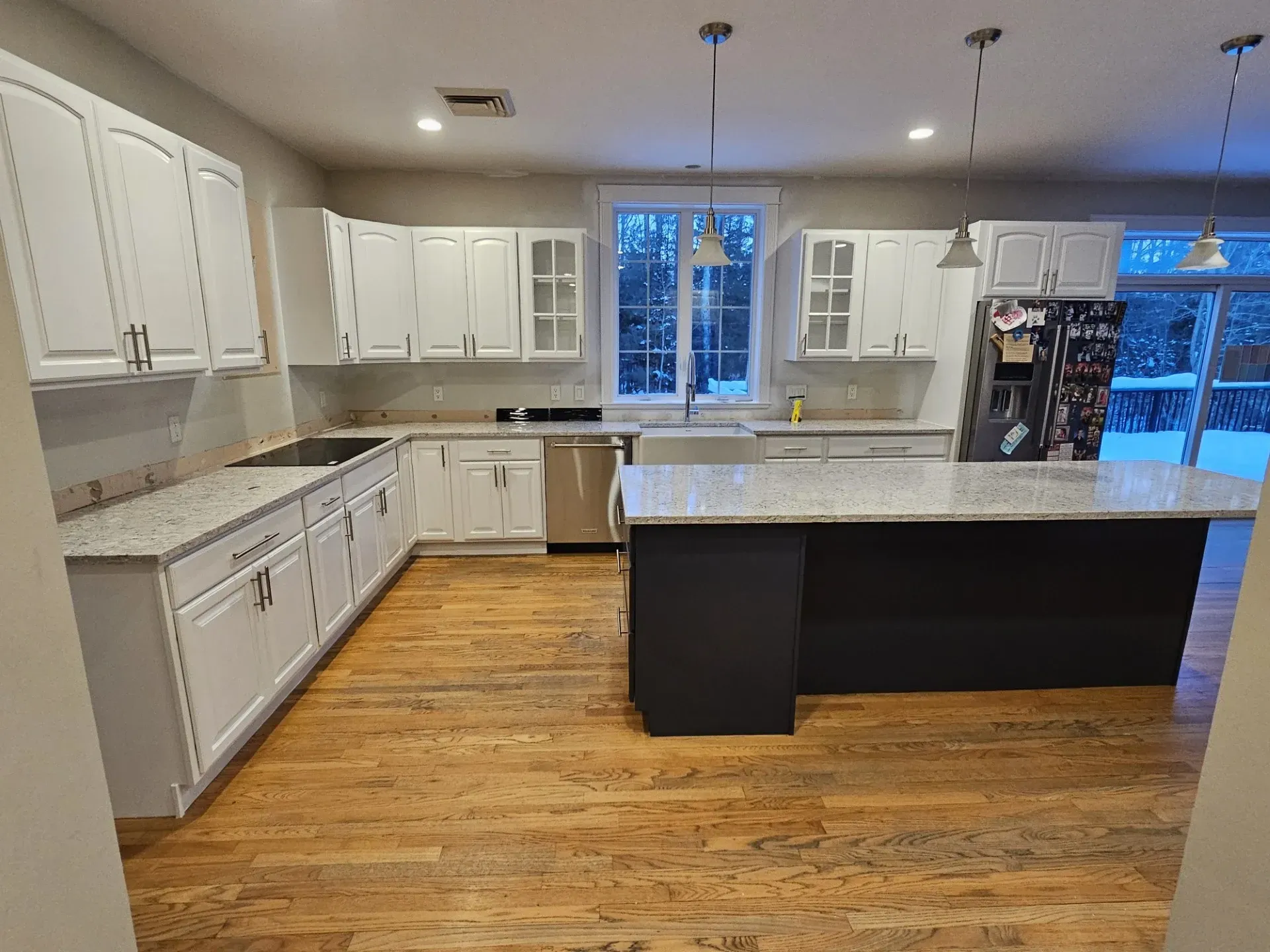 A bright kitchen featuring white cabinets, granite countertops, a dark island, and light hardwood floors.