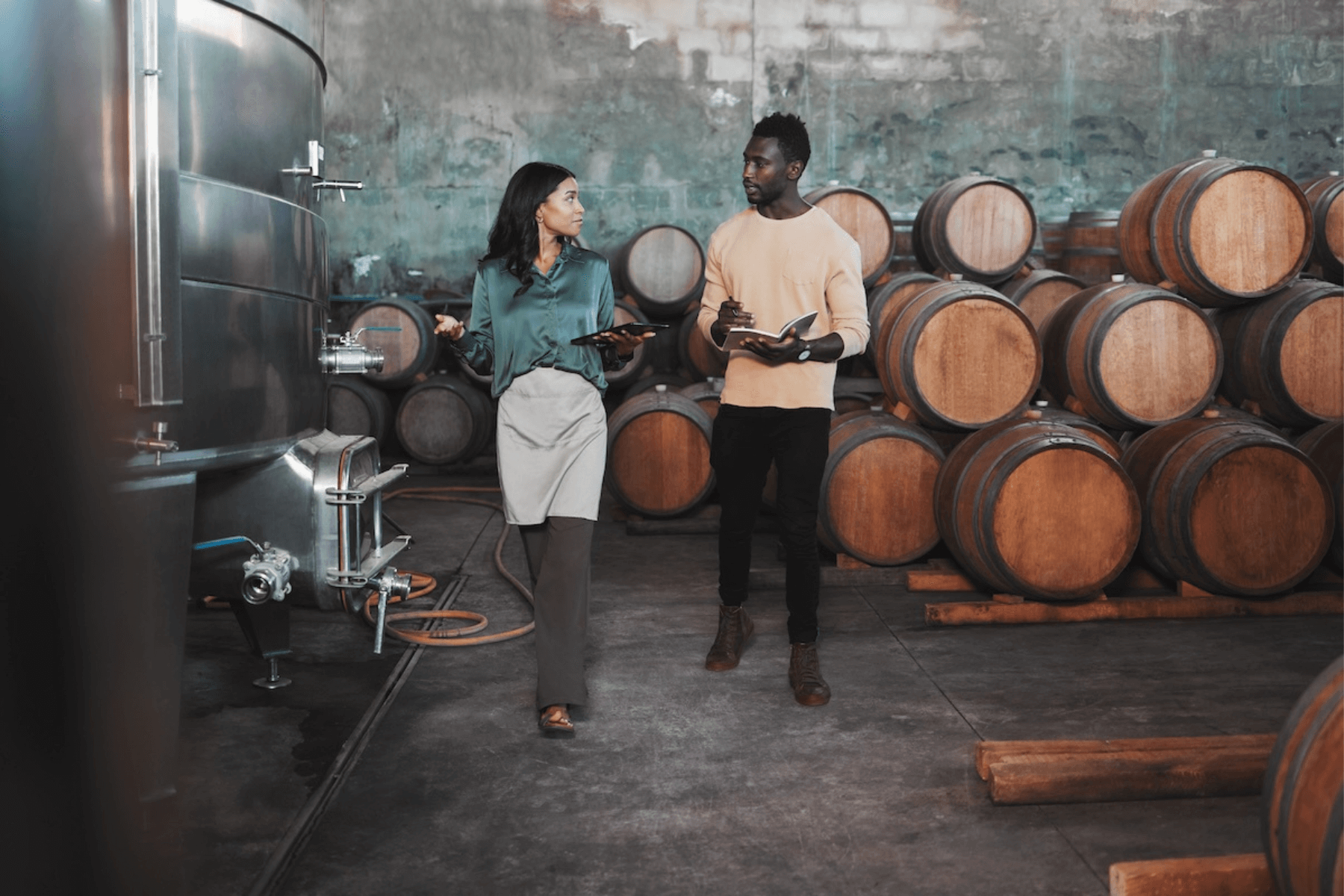 A man and a woman are standing next to each other in a wine cellar.