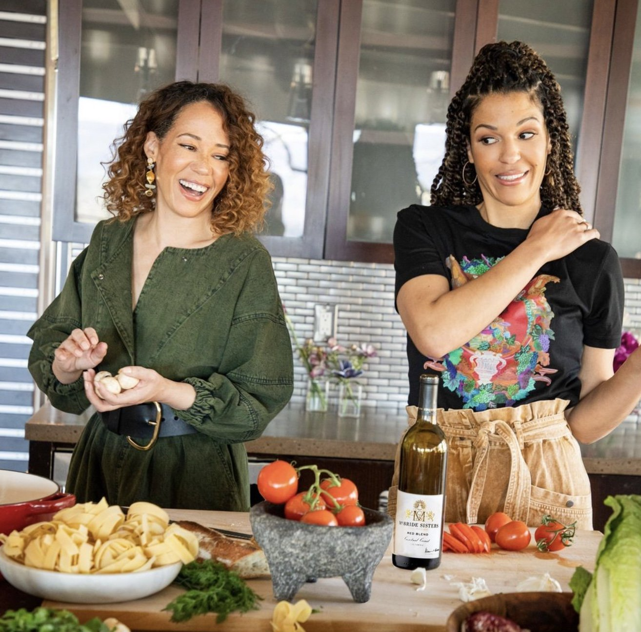 An image of Robin and Andréa McBride laughing together while preparing food at a wooden table.