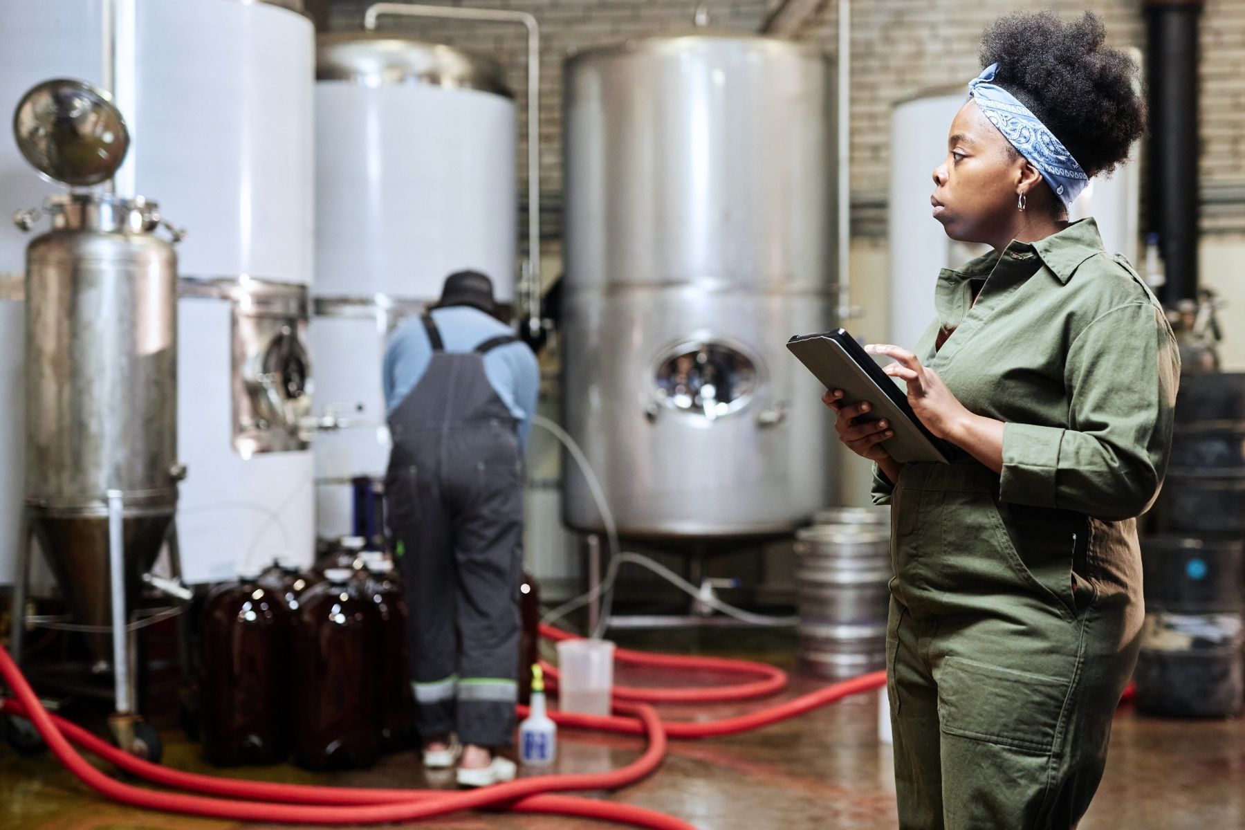 A woman is standing in a brewery looking at a tablet.