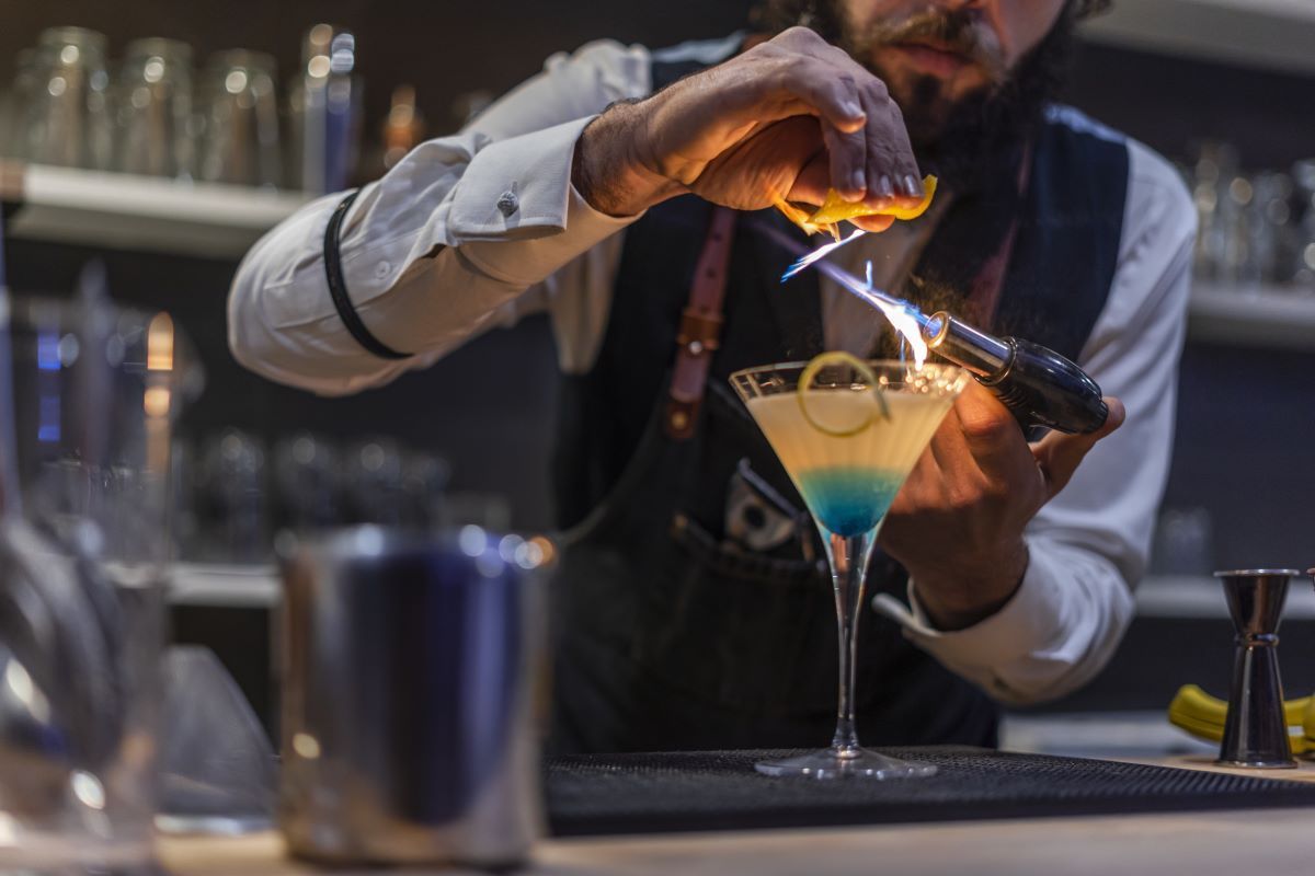 bartender making a cocktail in a martini glass with blue liquor and a hand torch