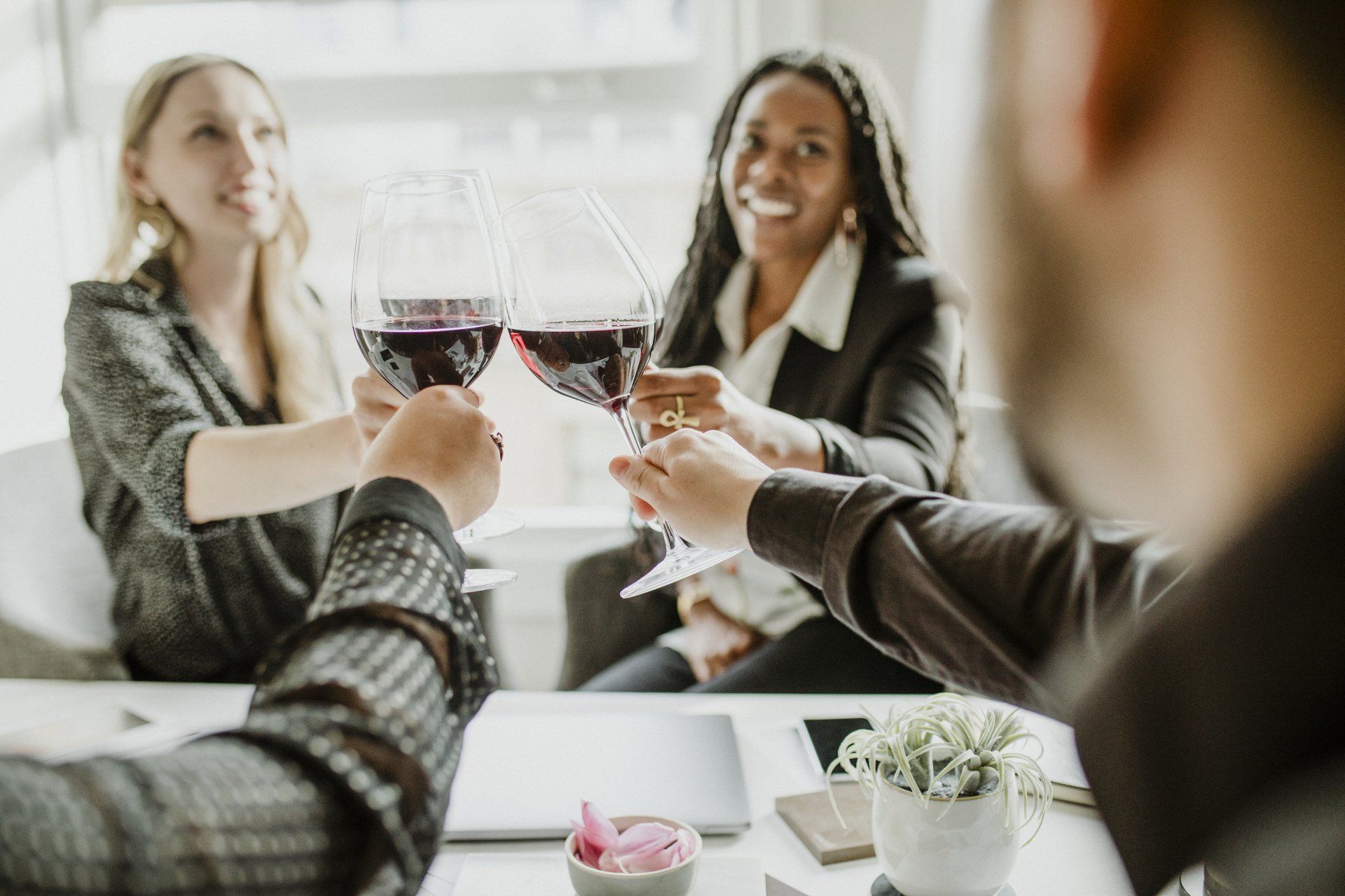 Image of a group of four business people clinking wine glasses over a white table.