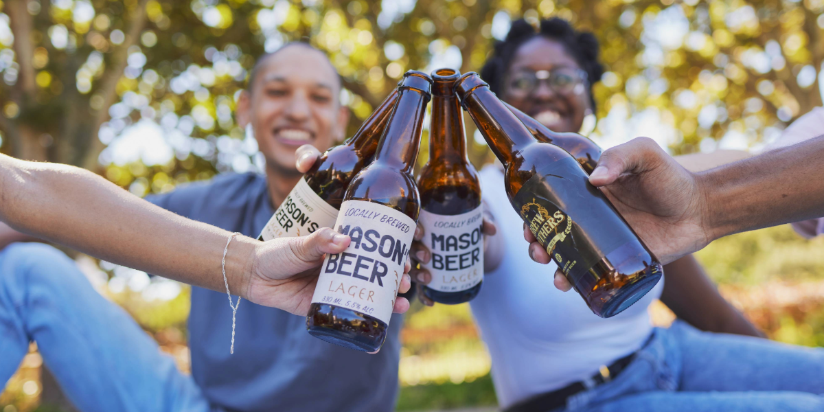 A group of people are holding bottles of beer in their hands having a picnic.