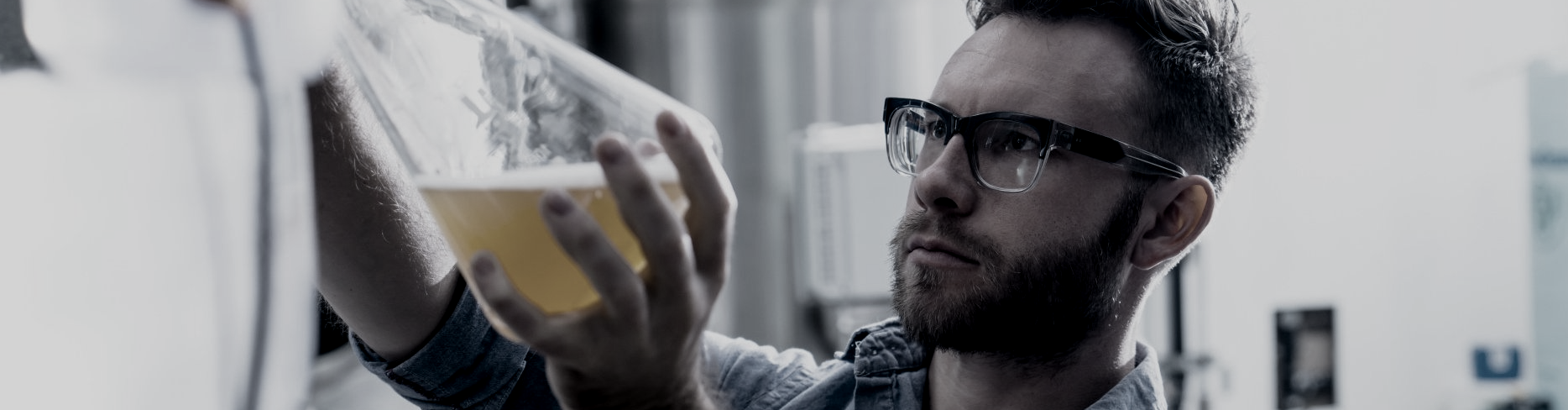 Young man with glasses examines a large beaker of beer.