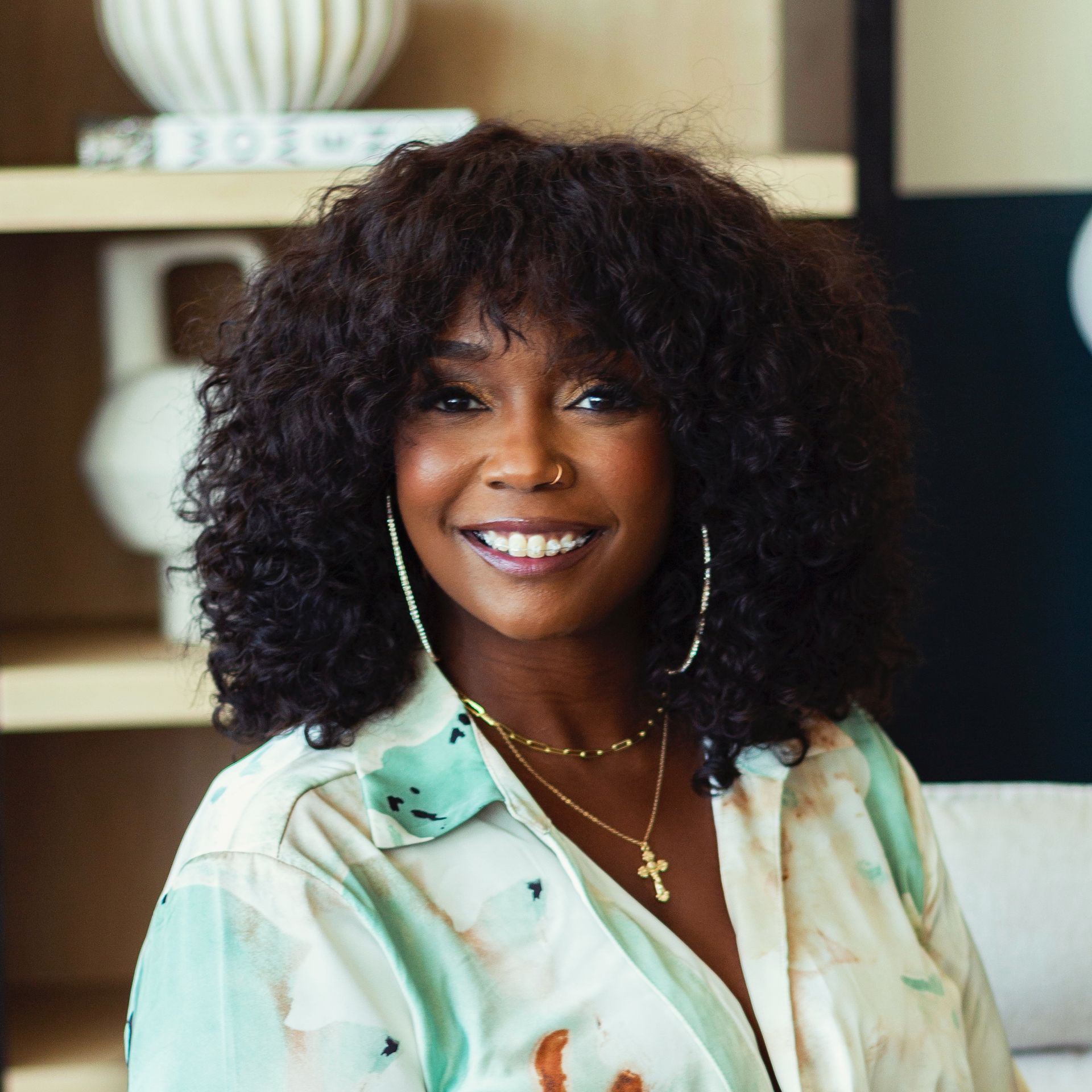 A woman with curly hair and a cross necklace is smiling for the camera.