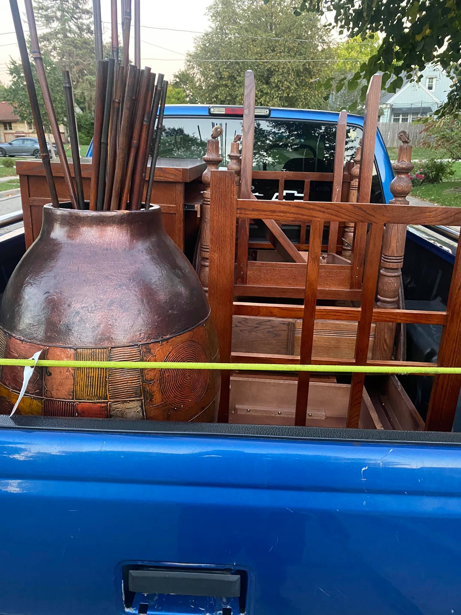 A blue truck is filled with wooden furniture and a lamp