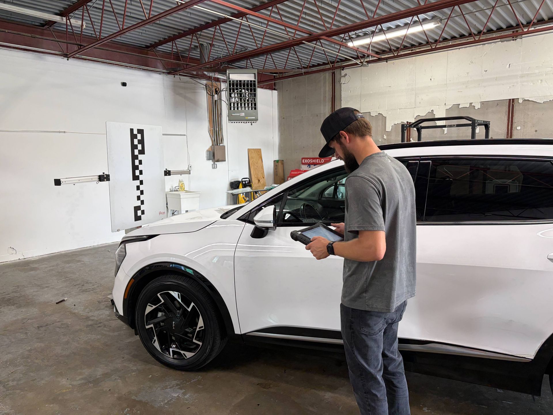 Man holding a device beside a white SUV in a garage with exposed ceiling beams