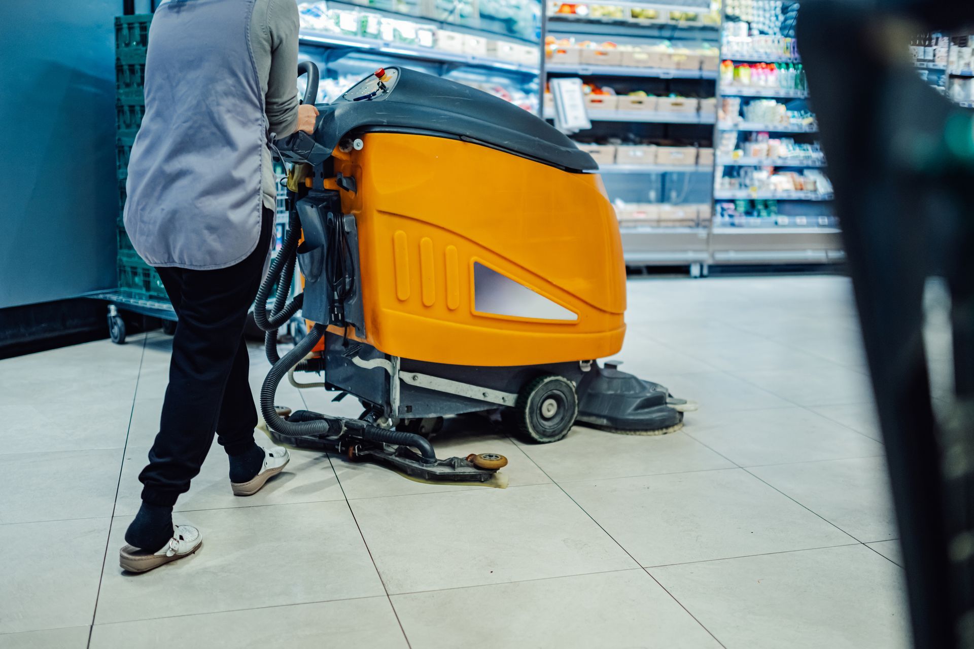 Female porter using a floor scrubber machine in a supermarket. Female porter using a floor scrubber machine in a supermarket.