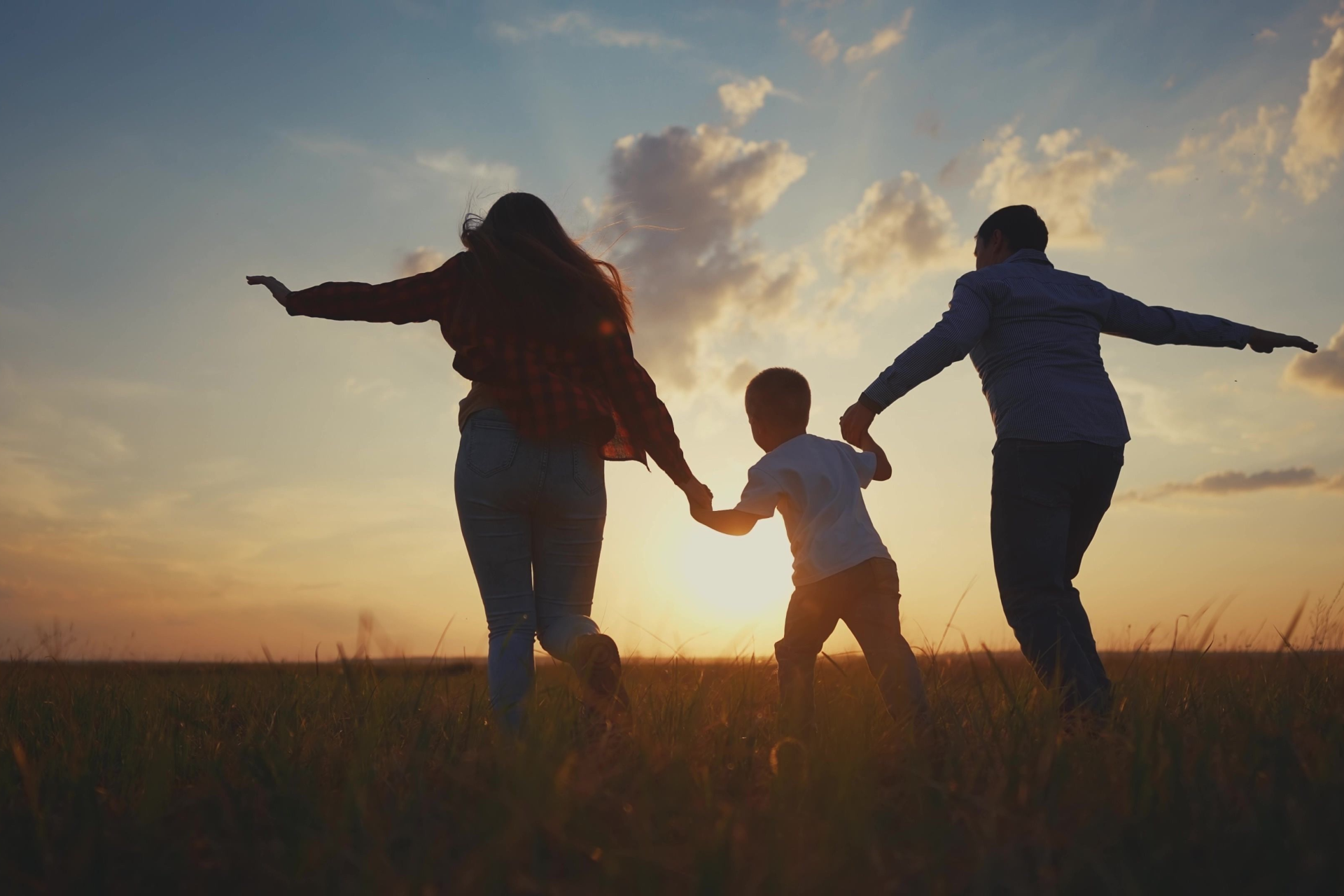 A family silhouette holding hands and running through a field during a golden sunset.