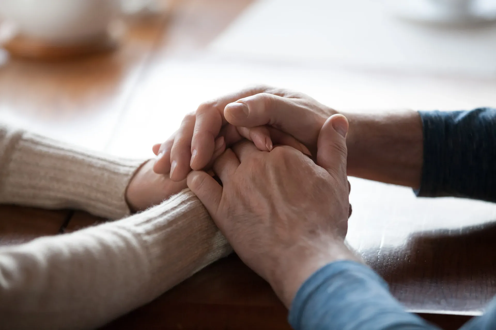 Two people holding hands across a wooden table, conveying comfort and support.