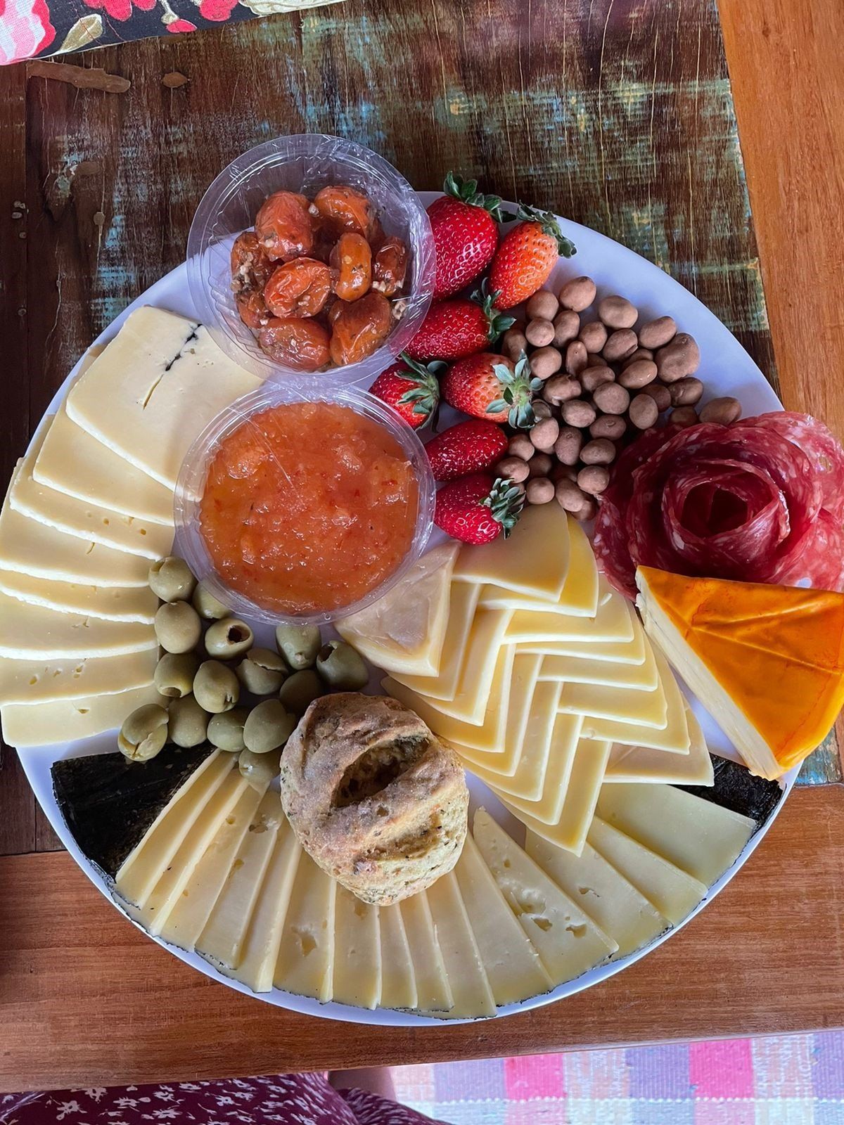 Um prato branco coberto com fatias de queijo, azeitonas, morangos e geleia.