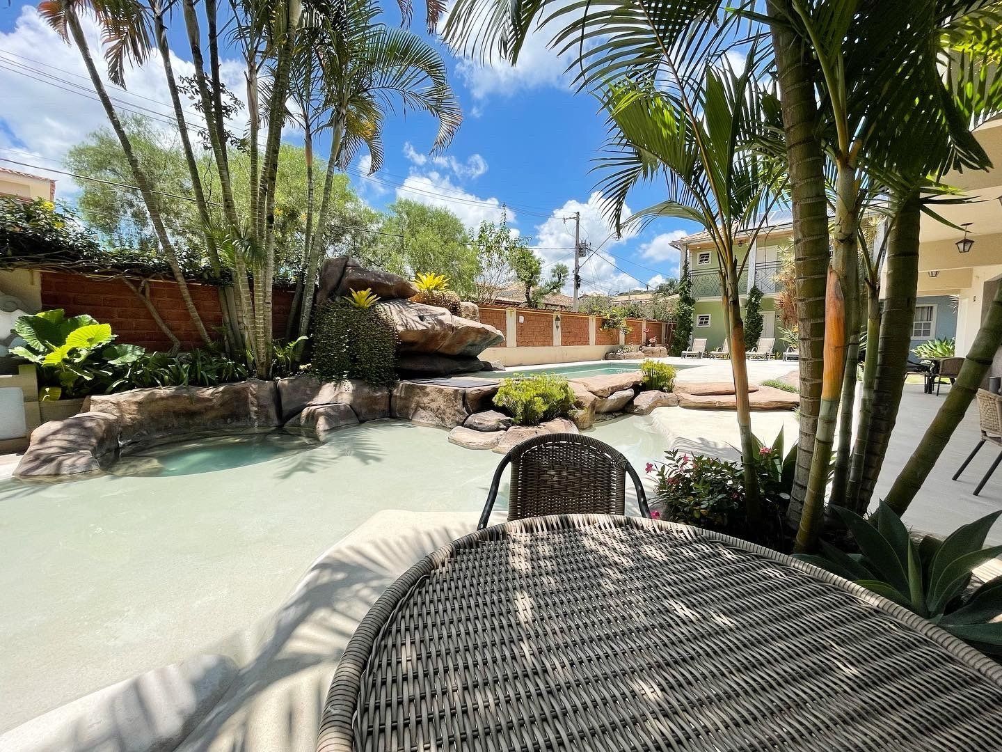 Uma mesa e cadeiras de vime estão ao lado de uma piscina cercada por palmeiras.