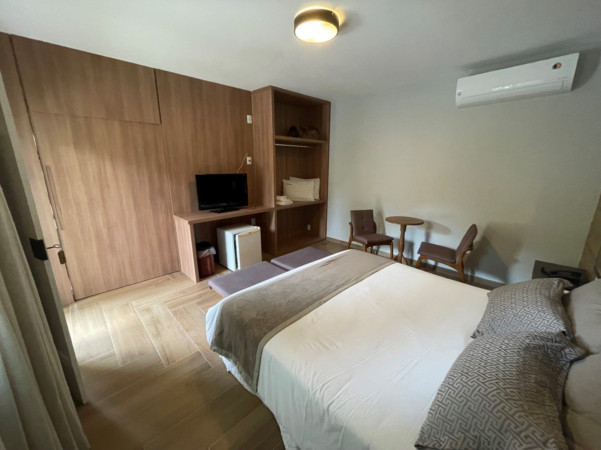 Um quarto de hotel com uma cama, cadeiras, uma televisão e uma geladeira.